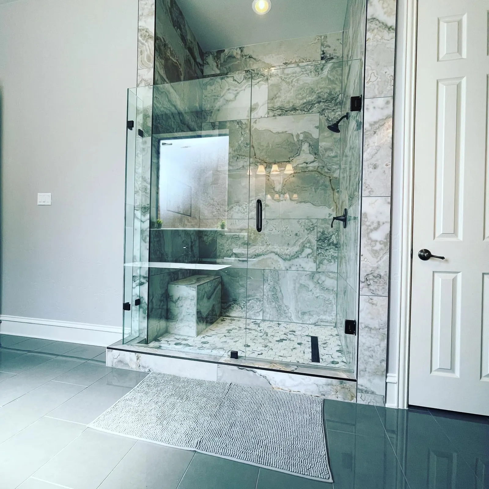 Frameless glass walk-in shower with marble slab walls and a built-in bench